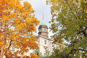 La tour dun btiment en briques visible entre deux arbres, dont lun a des feuilles oranges et lautre, des feuilles verdtres.