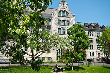 Un btiment dun campus universitaire en briques grises entour darbres et de verdure.