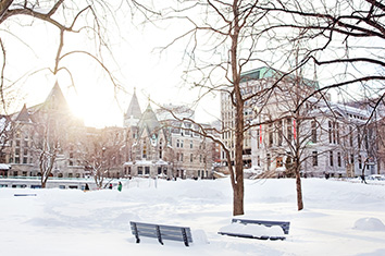 A snowy university campus with the sun visible over buildings