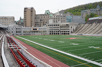 A football field surrounded by empty bleachers in front of a cityscape and a mountain.