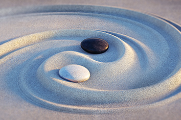 A black and a white stone form the centre points of a yin yang swept into the sand of a Zen Garden.