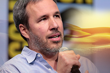 Un homme (Denis Villeneuve) en gros plan, assis devant une affiche non focalisée du Comic-Con