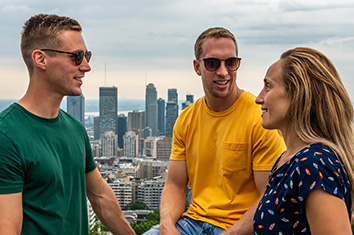 Deux hommes portant des lunettes de soleil et une femme se tiennent près l’un de l’autre au sommet du mont Royal à Montréal.