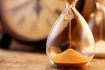 Des grains de sable tombent dans le vase inférieur d’un sablier devant une vieille horloge.