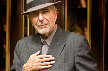 Un homme, Leonard Cohen, porte un costume gris et un chapeau, la main sur la poitrine.