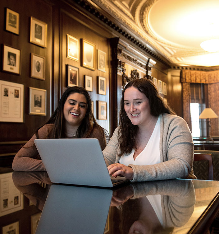 Two students work on a laptop in the Common Room of the Chancellor Day Hall Law building.